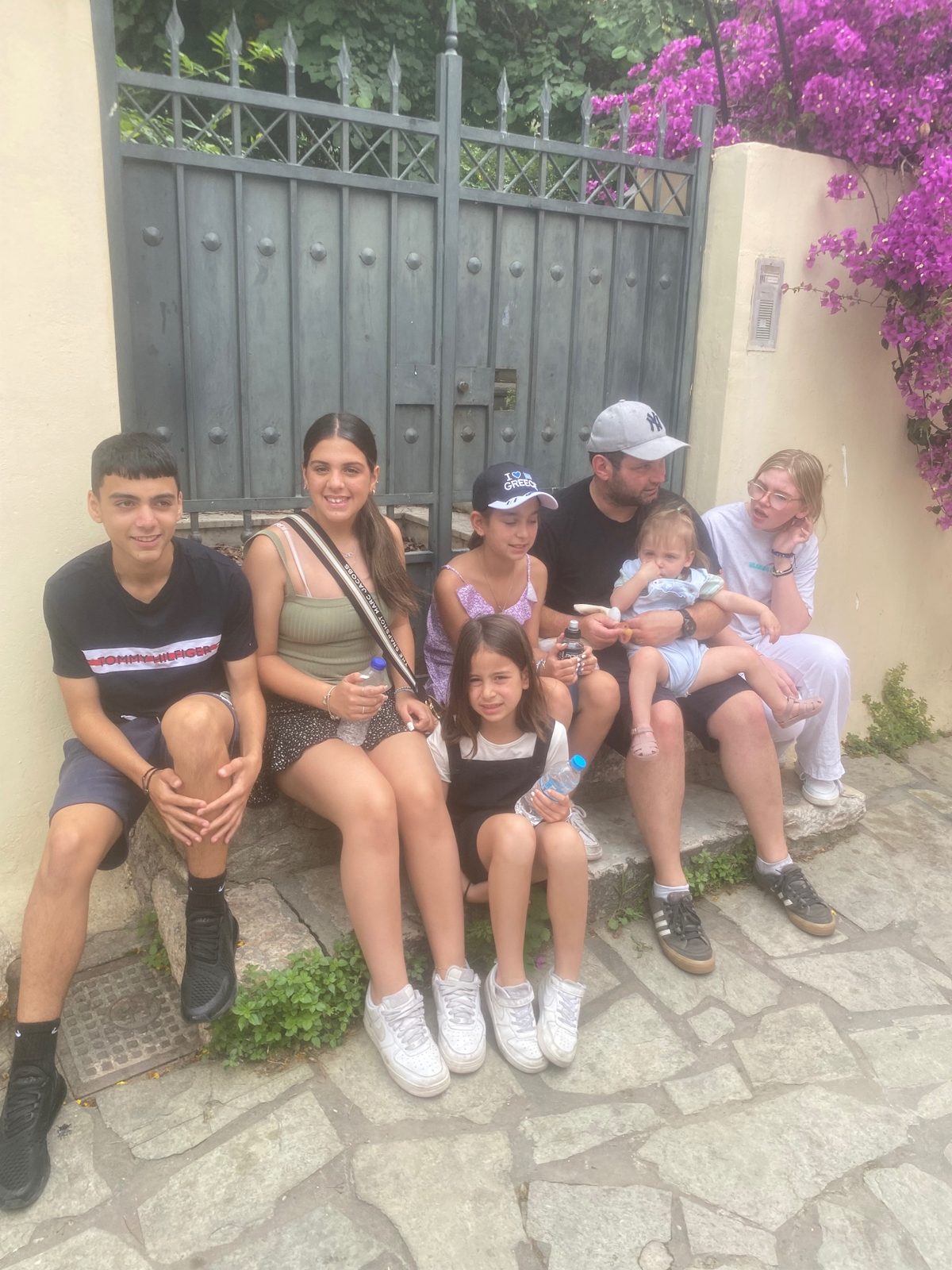 Our family sitting together on stone steps beside a bougainvillea-covered wall in Greece