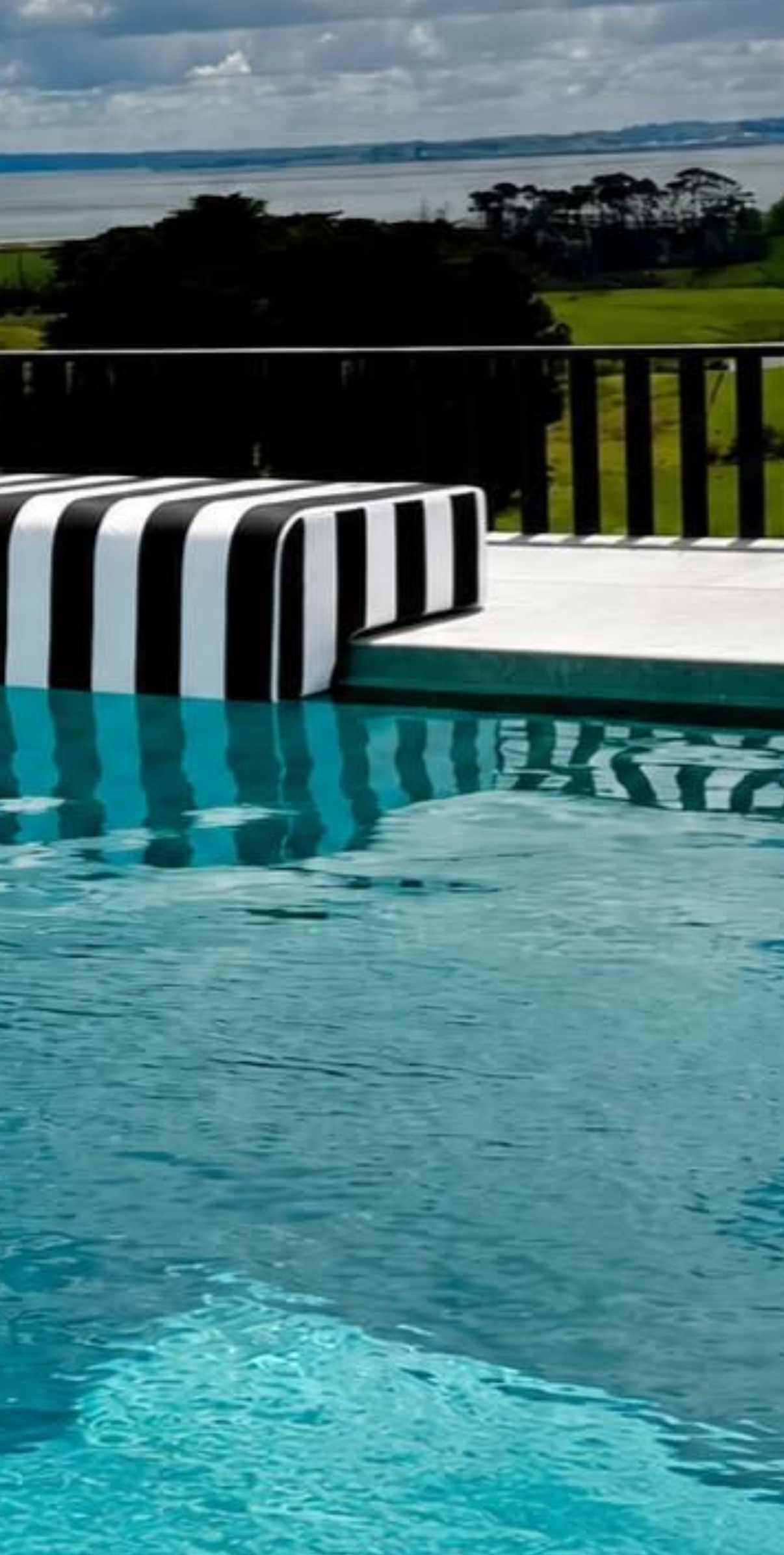 Close-up of a striped Akti cushion fitted to pool coping above clear blue water