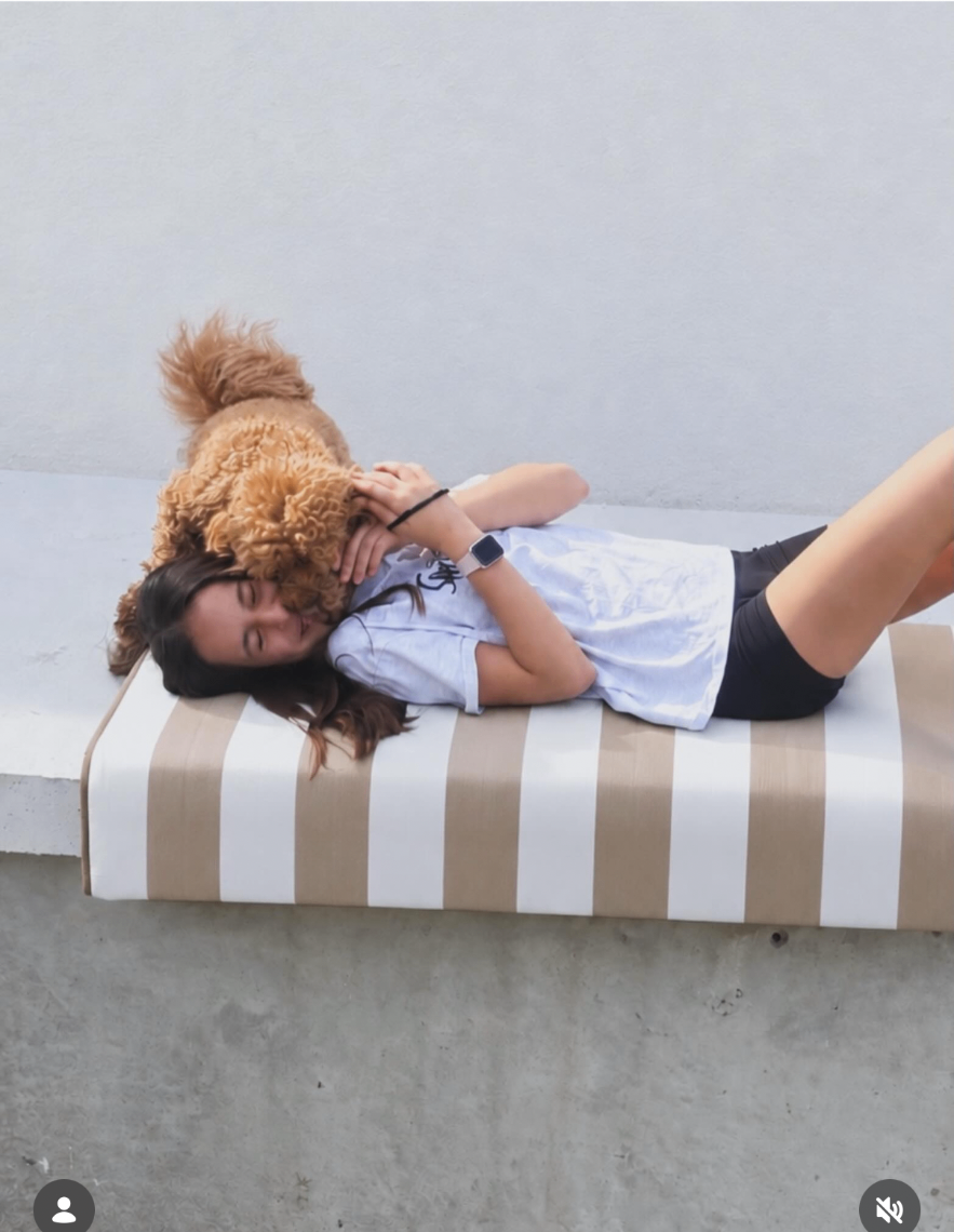 Akti cushion in a cream stripe used as a day bed by the pool, with a girl lying down cuddling her dog