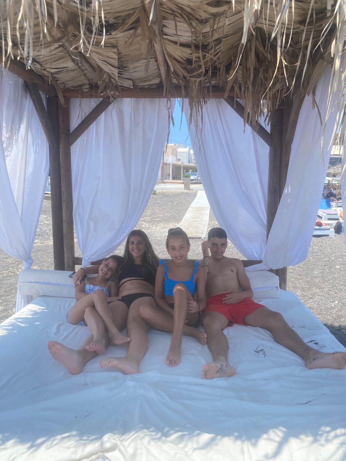 Four of the children relaxing on a white daybed under a thatched beach cabana