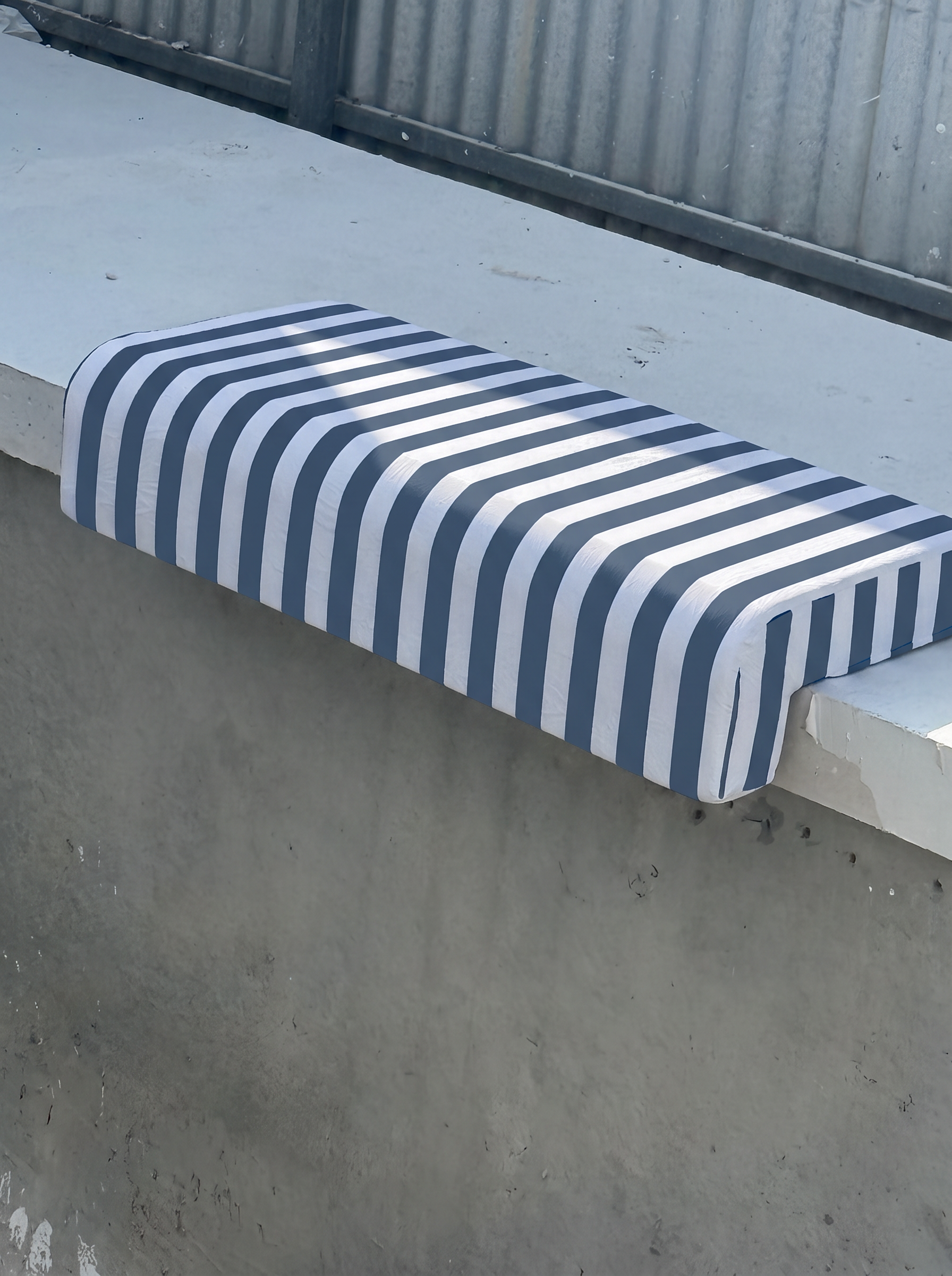 Aegean Blue and white striped Akti cushion fitted over white pool coping in full sun